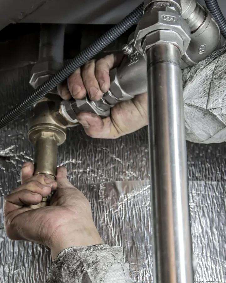 Plumber's hands tightening a compression fitting on a chrome waste pipe beneath a sink